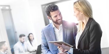 Man and woman are discussing in an office with people sitting on a desk